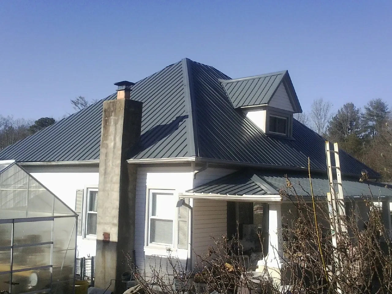Dark blue standing seam metal roof on a white farmhouse with dormer — Slate & Tile Roof Repair by Roofing Brothers in Saint Ignatius