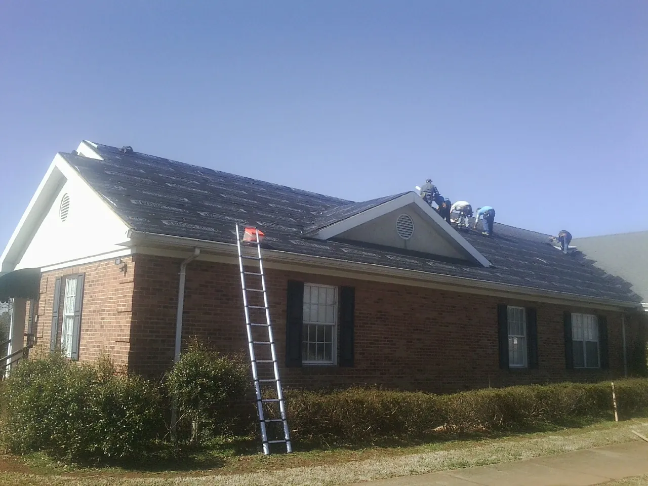 Crew tearing shingles off a brick ranch roof with a ladder set — Emergency Roof Repair work by our crew in Saint Ignatius