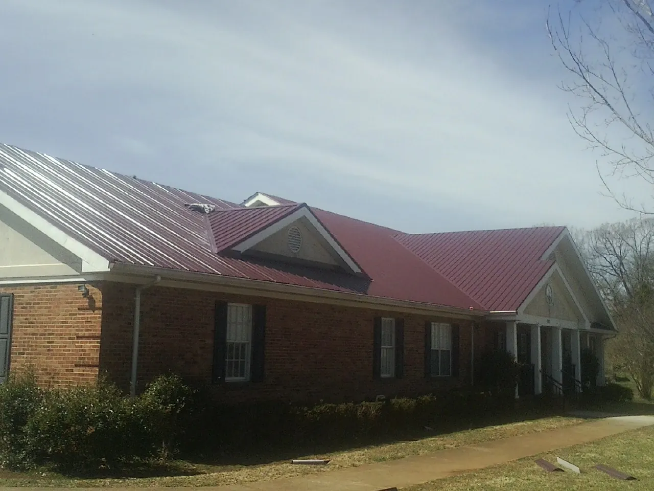 Red metal roof with gabled entries on a long brick building, from a Hail Damage Roof Repair job in Saint Ignatius
