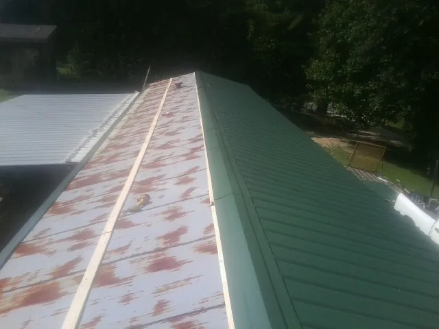 Old rusted panels beside newly installed green metal roofing — Wind Damage Roof Repair by Roofing Brothers in Saint Ignatius