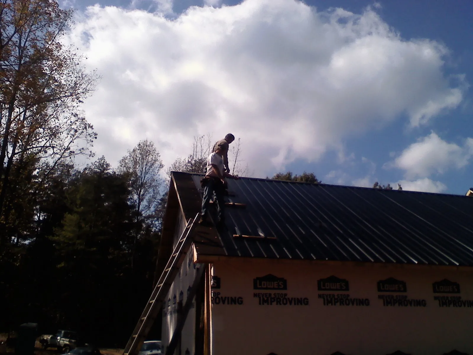 Roofer fastening dark metal panels high against a cloudy sky, from a Roof Inspection job in Saint Ignatius