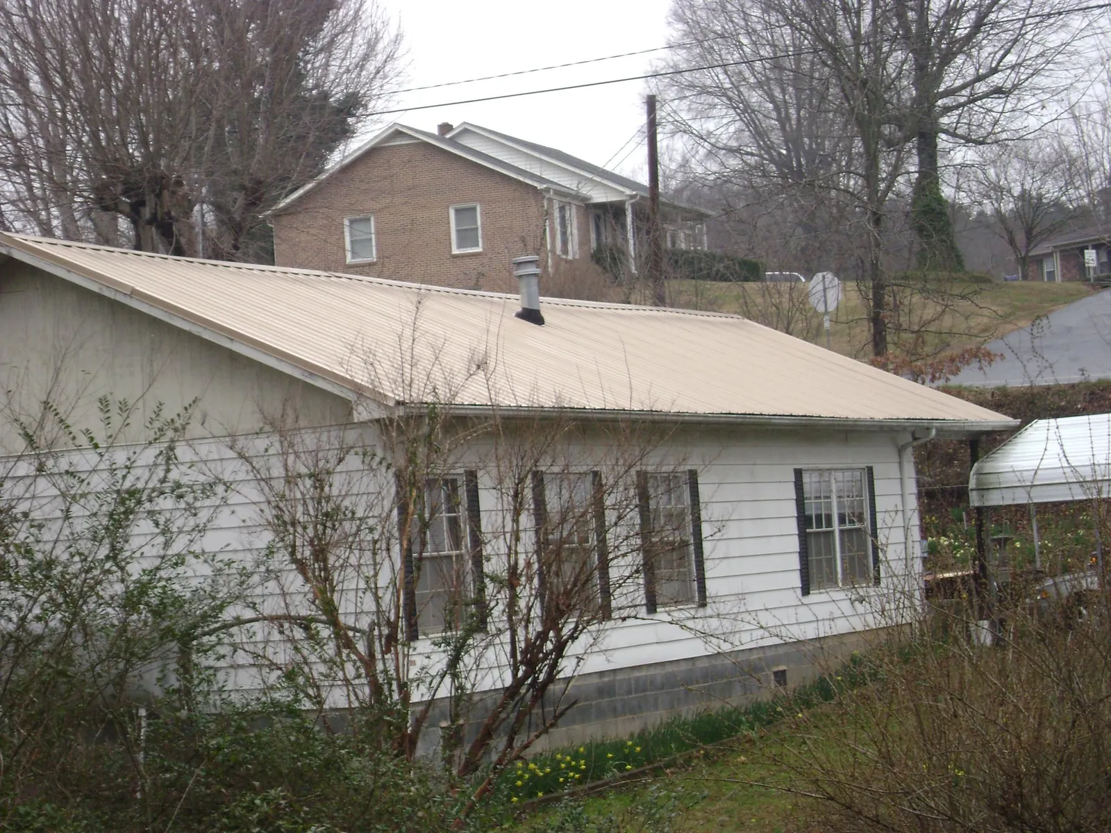Tan metal roof on a white sided house set into a hillside — Commercial Roofing by Roofing Brothers in Saint Ignatius