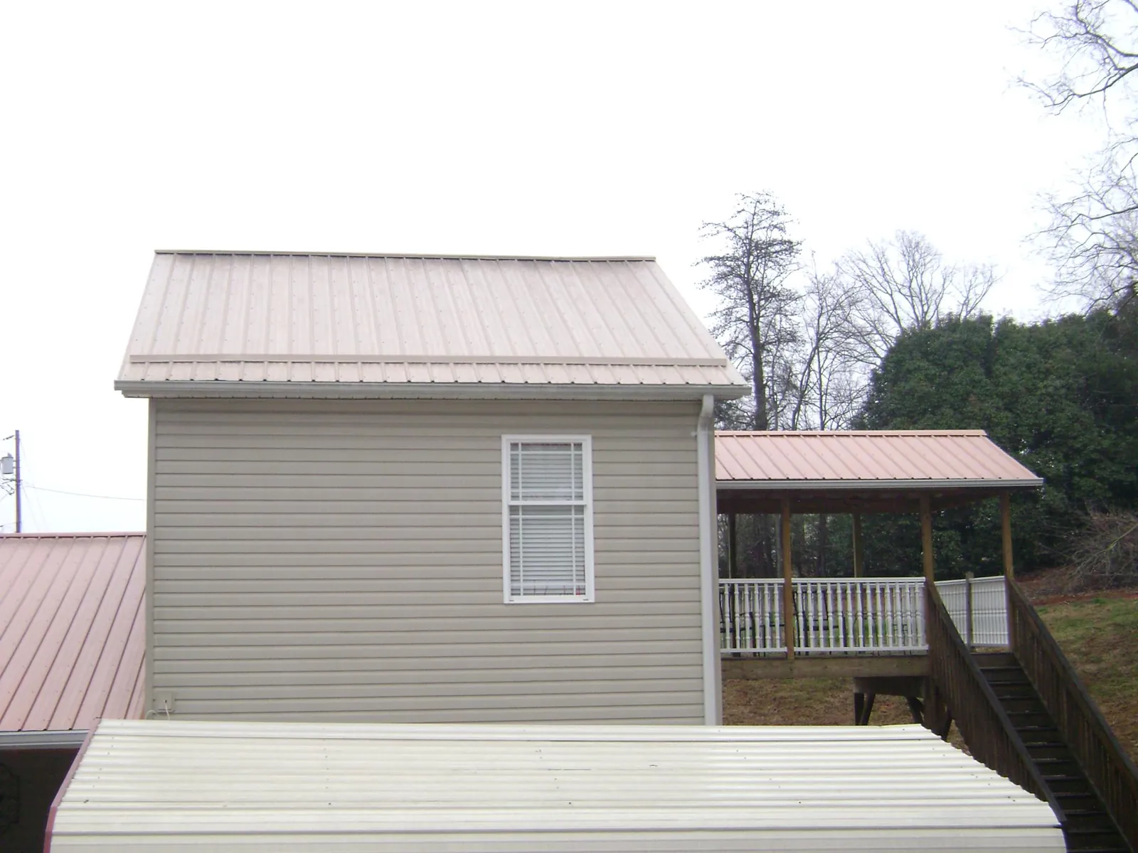 Tan metal roofs on a two story addition and attached porch, from a Roof Replacement job in Saint Ignatius